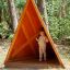 Child standing inside wooden Tipi Nature playhouse in forest setting