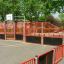 Outdoor basketball court with red and black fencing - Shea product.
