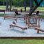 Wooden Sahara playground seesaw and spring rocker on sand surface in park area.