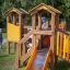 Alpha playhouse with slide on a grassy playground with children playing.
