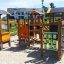 Alpha playhouse with slide in a sunny playground, surrounded by sand and residential buildings in th