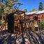 Wooden playhouse with climbing walls and slide in a playground setting.