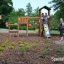 Triangle Modern Nature wooden playhouse with slide in a park setting with children playing.
