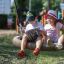Two children sitting on a Nature Swing Frame BNS+1 (multiple swing) outdoors.