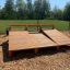 Sit-ups Bench made of wooden planks, placed outdoors on a wood chip surface, with greenery and trees