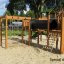 Romping Cottage - wooden playground structure with climbing elements and slide on sandy ground