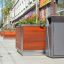 Chicago bin next to a large wooden planter on a city sidewalk.