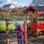 Child playing with Abacus playground equipment next to a wooden playhouse outdoors.