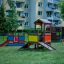 Colorful wooden playhouse with slides and climbing frames in a grassy area surrounded by apartment b