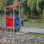 Neptune single playhouse with red roof and blue panel in a playground.