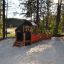 Locomotive with cars train playhouse in a sandy playground surrounded by trees.