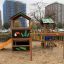 Jungle House playhouse with slide on a playground with city buildings in the background.
