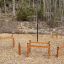 Outdoor Trim trail wooden exercise equipment set up in a forest clearing on wood chip ground.
