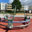 Bicycle merry-go-round at a playground with apartment buildings in the background.