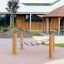 Obstacle Course Crawl Net suspended between wooden posts on playground with modern building in backg