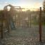 Challenger Modern Nature wooden playground set with slide on sandy ground at sunset.