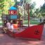Children playing on a ship-shaped sandbox in a park.
