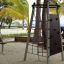 Spinner I playground climbing structure on a sandy beach with palm trees in the background.