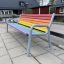 Colourful bench with rainbow slats and metal frame on outdoor pavement.