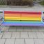 Colourful bench with rainbow-coloured slats and metal frame on playground pavement.