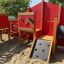 Barn playground equipment with climbing wall and interactive panels on sandy ground