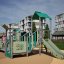 Fortress with a slide playground structure with climbing elements and green slide on soft safety sur