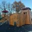 Wooden Scandinavian stronghold playground structure with slide and climbing wall.