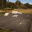 Skate park with curb sloping height 15-25cm ramps and rails on asphalt surface in a grassy area.