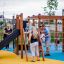 Children and adults playing on the Little Jungle Nature playground equipment in a park.