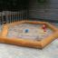 Hexagonal sandbox with bark frame and toys.