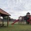Firehouse playground structure with red slides and wooden climbing frames in a park.