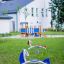 Bird swing rocking on a grassy playground in front of a white building