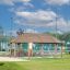 Wooden Long Firehouse playground shelter with benches on a grassy area under a blue sky.