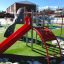 Whale - AZTEC steel structure playground with red slide and climbing walls on a green lawn.