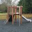 Wooden playground structure Yosemite with a slide and climbing net in a fenced outdoor play area.