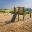 Kampinos wooden playhouse in a sandy outdoor playground by the sea.