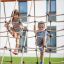 Children climbing on a Nature Ship Sandbox, wooden playhouse rope net.