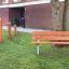 Triple Somersault Nature playground near brick building with wooden bench and outdoor gym equipment.