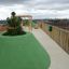 Playground area on a rooftop with Wetpour 100 green safety surface and wooden play structures.