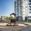 Outdoor Playhouse Nature in a sandy playground with tall apartment buildings in the background.