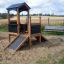 Playhouse Nature in a sandy playground with a bench in the background.
