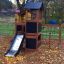 Wooden playhouse with slide in a playground surrounded by autumn leaves.