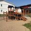 Tower Nature wooden playhouse with slide on sandy playground.