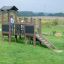 Fortress Nature playhouse with slide in a green field with a child playing.