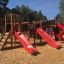 Playground structure Mastodon castle with slide, featuring red slides and wooden climbing elements.