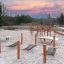 Black net hammock on wooden frame at sandy playground under colourful evening sky.