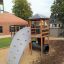 Six Angle Aztec wooden playground structure with climbing wall and slide in a school yard.