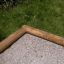 Wooden corner of the 5-angle palisade sandbox on the grass.