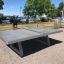Concrete table tennis, free-standing on outdoor patio near water.