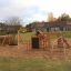 Panther wooden playhouse in a sandy playground with swing and climbing wall.